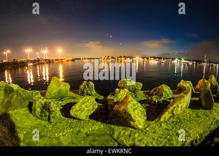 Port Washington, New York, Stati Uniti d'America. Il 26 giugno 2015. Al di là delle rocce del litorale parete lungo Sunset Park, di notte le luci sfarfallano sulle Manhasset Bay in Gold Coast di North Shore Long Island. Credito: Ann e Parry/Alamy Live News Foto Stock