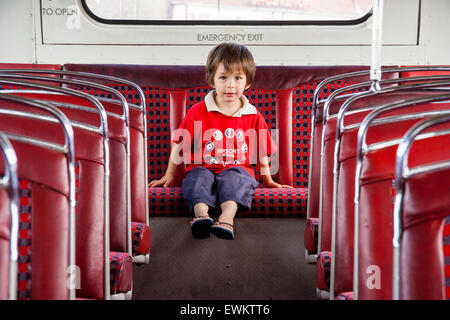 Bambino caucasico, boy, 3-4 anni seduto da solo sul sedile posteriore di un autobus di Londra, teleobiettivo shot attraverso la sede del corridoio della di lui guardando il visualizzatore. Foto Stock