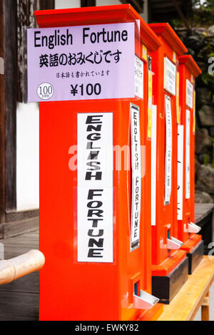 Fila di tre rossi distributori automatici per il giapponese fortune scivola, o-mikuji presso il Tempio Dorato a Kyoto. Segno indicante la slitta sarà in lingua inglese. Foto Stock