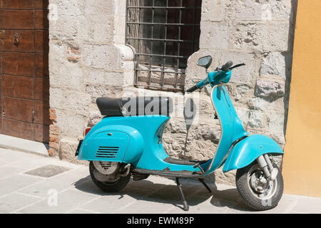 Luminose aqua blue scooter parcheggiato nel villaggio italiano sotto la strada sbarrata finestra nel muro di pietra. Foto Stock
