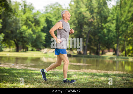 Profilo di colpo un attivo senior jogging in un parco e ascolto di musica sulle cuffie Foto Stock