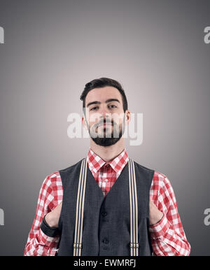 Dissaturato Ritratto di giovane barbuto hipster con mani spinto nella sua vest su grigio scuro di sfondo per studio con vignette. Foto Stock