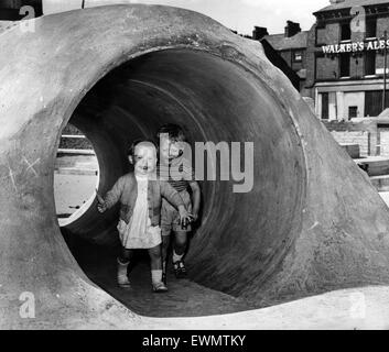 Due giovani bambini che si divertono in esecuzione attraverso un tunnel di cemento in un parco giochi avventura. 2 Giugno 1966. Foto Stock