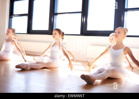 Gruppo di carino piccolo leggiadre ballerine nella classe di seduta sul pavimento in legno dello studio praticando una posa con proteso Foto Stock