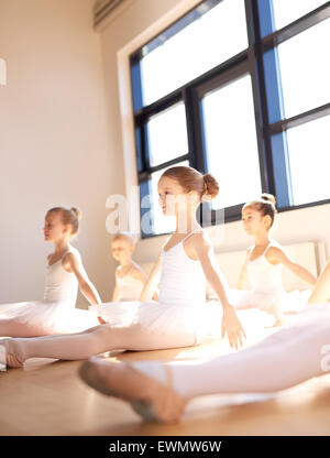 Classe di giovani ballerine praticando insieme in un luminoso monolocale soleggiato seduta sul pavimento di legno in un grazioso pongono, bassa angl Foto Stock