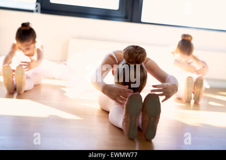 Un gruppo di giovani ballerini nella classe facendo esercizi di stretching seduti sul pavimento di legno come si scaldano prima della pratica in incr Foto Stock