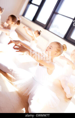 Graziosa ragazza di balletto in bianco Tutu, facendo un esercizio di stiramento, con le gambe aperte e le braccia in avanti, all'interno di Studio con lui Foto Stock