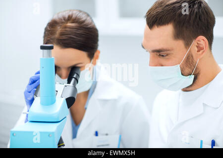 Gli scienziati nelle maschere guardando al microscopio in corrispondenza di lab Foto Stock