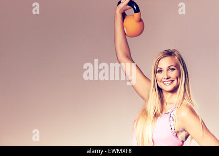 Giovane donna che indossa abiti da allenamento sorridente alla videocamera e sollevare un kettlebell. Foto Stock