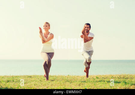 Coppia sorridente facendo esercizi di yoga all'aperto Foto Stock