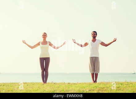 Coppia sorridente facendo esercizi di yoga all'aperto Foto Stock