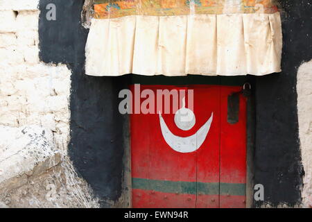 Dipinto di rosso-tradizionale stile tibetano-porta in legno incorniciata in nero con uno strano simbolo bianco tessuto sotto la tettoia. Gyantse-Tibet. Foto Stock