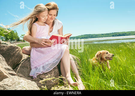 Bambina con la madre la lettura di un libro in un parco estivo Foto Stock