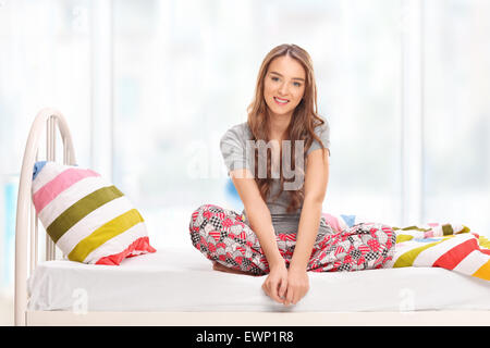 Bruna giovane donna in pigiama seduto su un letto e guardando la telecamera a casa Foto Stock