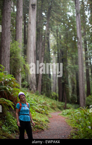 Ritratto di una donna in piedi su un sentiero tra gli alberi alti. Foto Stock