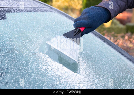 Mano indossando guanti di graffiare il ghiaccio dal finestrino con gelo in inverno Foto Stock