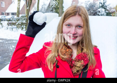 Giovane donna caucasica vestito di rosso tenendo palla di neve a buttare in inverno Foto Stock