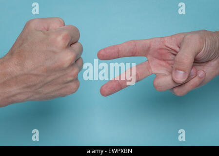 Gli uomini con le mani in mano e suona rock, Paper, Scissors su sfondo azzurro. Uno è di gettare il rock, l'altra è gettare le forbici. Foto Stock