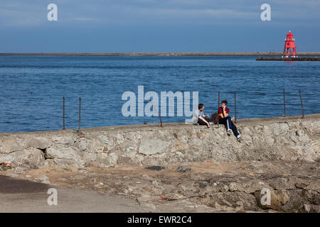 Due ragazzi adolescenti a sedersi su un molo e la chat sul fiume Tyne a North Shields, un rosso luce di navigazione in background, Newcasstle Foto Stock