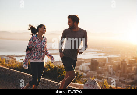 Coppia giovane correndo insieme all'esterno. Felice giovane uomo e donna jogging sulla strada di campagna durante il sunrise. Due persone godendo di mo Foto Stock