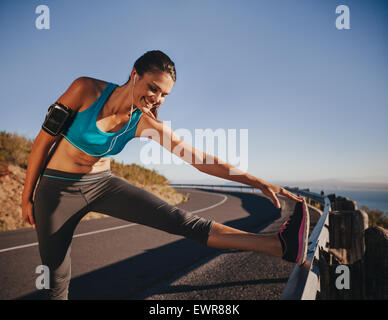 Sport donna stretching la gamba su una barriera di sicurezza prima di eseguire all'esterno. Atleta femminile ottenere pronto per una corsa. Foto Stock
