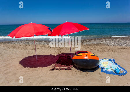 Due ombrelloni rossi sulla spiaggia di Rethymno, Creta, Grecia ombrelloni da spiaggia gettano un'ombra, ancora vita sulla spiaggia Gommone e asciugamani, nessuno Foto Stock