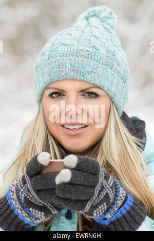 Giovane Bella Donna sorridente con la tazza di una bevanda calda all'aperto. Pretty girl holding tazza di caffè con boschi innevati dietro Foto Stock