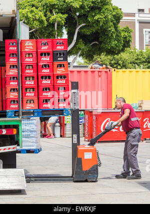 Driver di consegna lo scarico di pallet di Coca Cola con azionato a mano carrello. Foto Stock