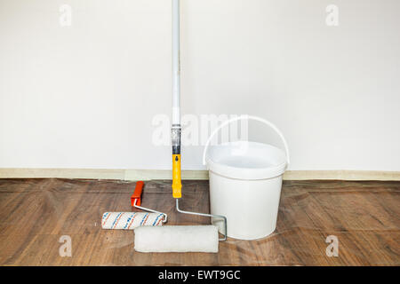 Due rulli di verniciatura e benna con una vernice bianco pronto per la verniciatura di pareti in una stanza Foto Stock