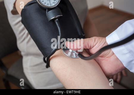 Medico cardiologo è di misurare la pressione sanguigna di donna nella sala di consultazione. Egli sta cominciando e sarà attento a notare Foto Stock