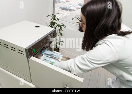 Giovani femmine dentista luoghi Medical autoclave per la sterilizzazione chirurgica e altri strumenti Foto Stock