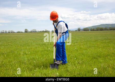 Lavoratore in tute è scavare con una pala, in un prato verde. Egli è in fase di avvio un nuovo progetto di costruzione. L'immagine è stata shoote Foto Stock