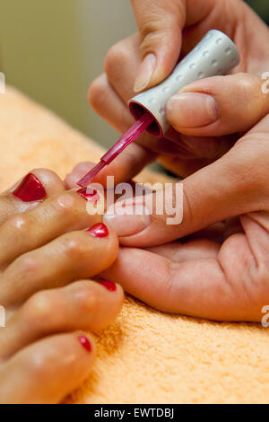 Close-up di pedicurist applicando red Nail Polish per la toenails, il fuoco selettivo Foto Stock