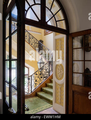 Vista attraverso il vetro aperto lo sportello pannellato con ritaglio fuori scala con ringhiera in ferro e pareti in stucco Foto Stock