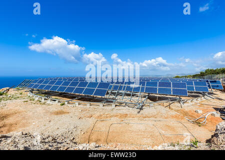 Campo di molti pannelli solari in righe sulla tavola girevole di costruzioni di metallo vicino al mare blu in Grecia Foto Stock