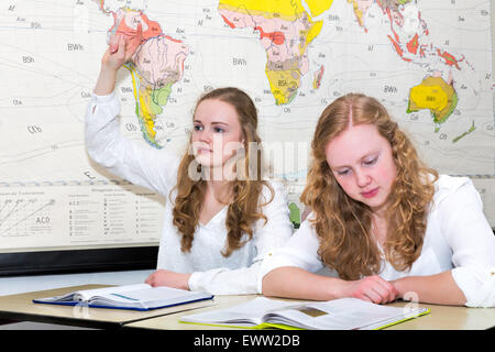 Caucasian ragazza adolescente e studente di imparare un dito nella lezione di geografia nella parte anteriore del diagramma a parete del mondo Foto Stock