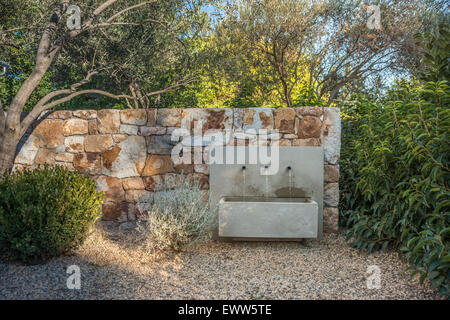 Giardino Fontana acqua montata sul muro di pietra naturale ombreggiati da alberi Foto Stock