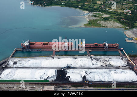 VISTA AEREA. Stoccaggio del carbone e del minerale di ferro (sotto la cellulosa bianca per prevenire gli inquinanti atmosferici). Ankaran (alias Ancarano, il suo nome italiano). Slovenia. Foto Stock