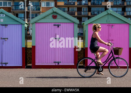 Un ciclista passa di pittoresca spiaggia di capanne sul lungomare di Brighton, Brighton, Sussex, Regno Unito Foto Stock