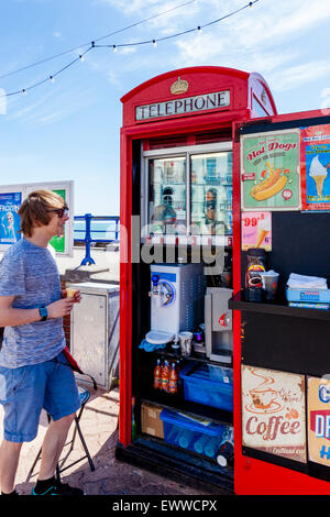 Un uomo serve gelati da un Convertito vecchio telefono rosso scatola, Eastbourne, Sussex, Regno Unito Foto Stock