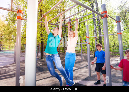 Gli adolescenti appendere sulla barra orizzontale presso gli sport di terra Foto Stock