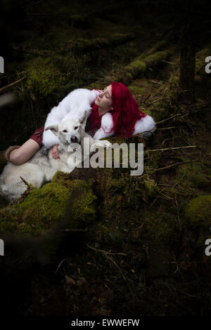 La roba di sogni e incubi: un giovane dai capelli rossi donna caucasica bambina da sola dormire in un buio pineta con un lupo bianco-come cane Foto Stock