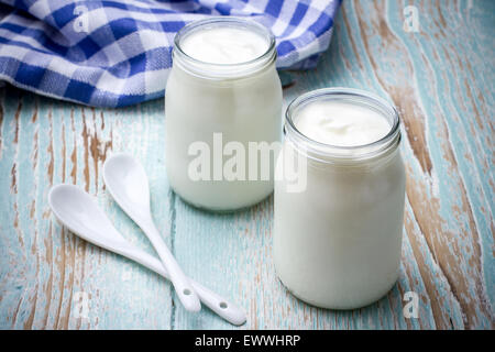 Due yogurt vetro sul piatto di legno con cucchiaino Foto Stock