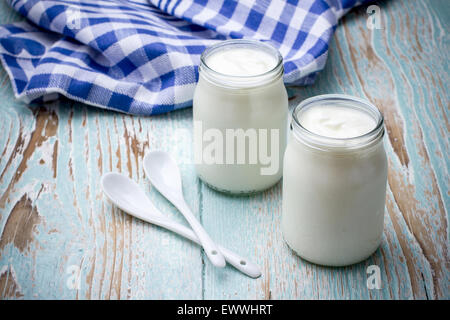 Due yogurt vetro su tavola di legno con cucchiaio in ceramica Foto Stock