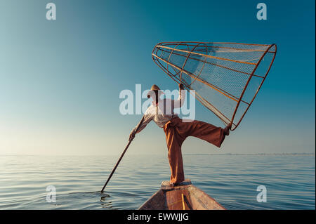 Pescatore birmano sulla barca di bambù per la cattura di pesce in modo tradizionale con la rete a mano. Lago Inle, Myanmar (Birmania) corsa destinat Foto Stock