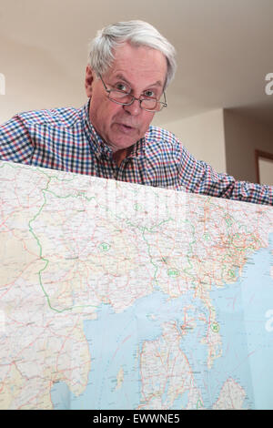 Senior cittadino in possesso di una mappa di Europa che guarda in telecamera Foto Stock