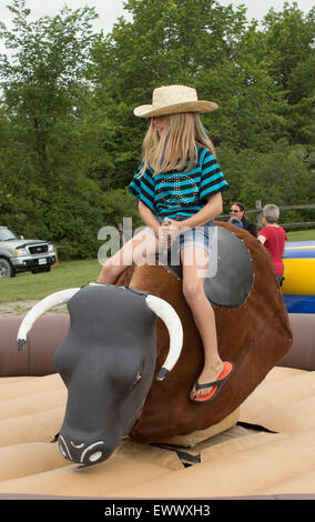 Giovani pre-teen ragazza cavalca un toro meccanico in Canada alle celebrazioni del Giorno in Cannington, Ontario Foto Stock