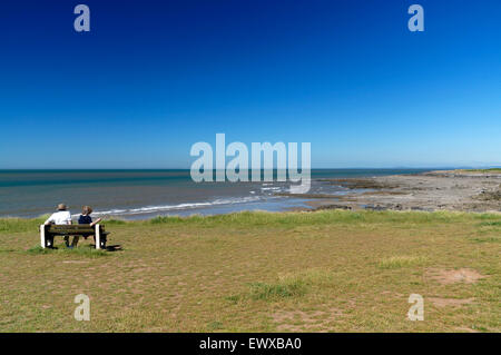 Coppia seduta sul banco di lavoro con vista della spiaggia, Porthcawl, South Wales, Regno Unito. Foto Stock