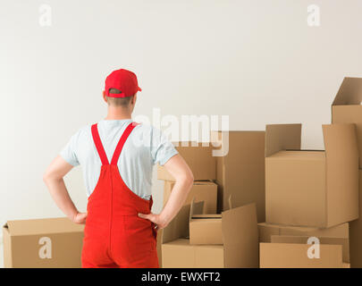 Vista posteriore del deliveryman piedi, guardando le scatole di cartone davanti a lui Foto Stock