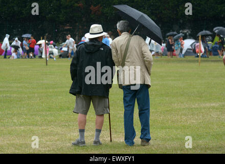 Due anziani signori riparo sotto un ombrello a guardare la gente in coda sotto la pioggia per Wimbledon Biglietti a Wimbledon Park Foto Stock
